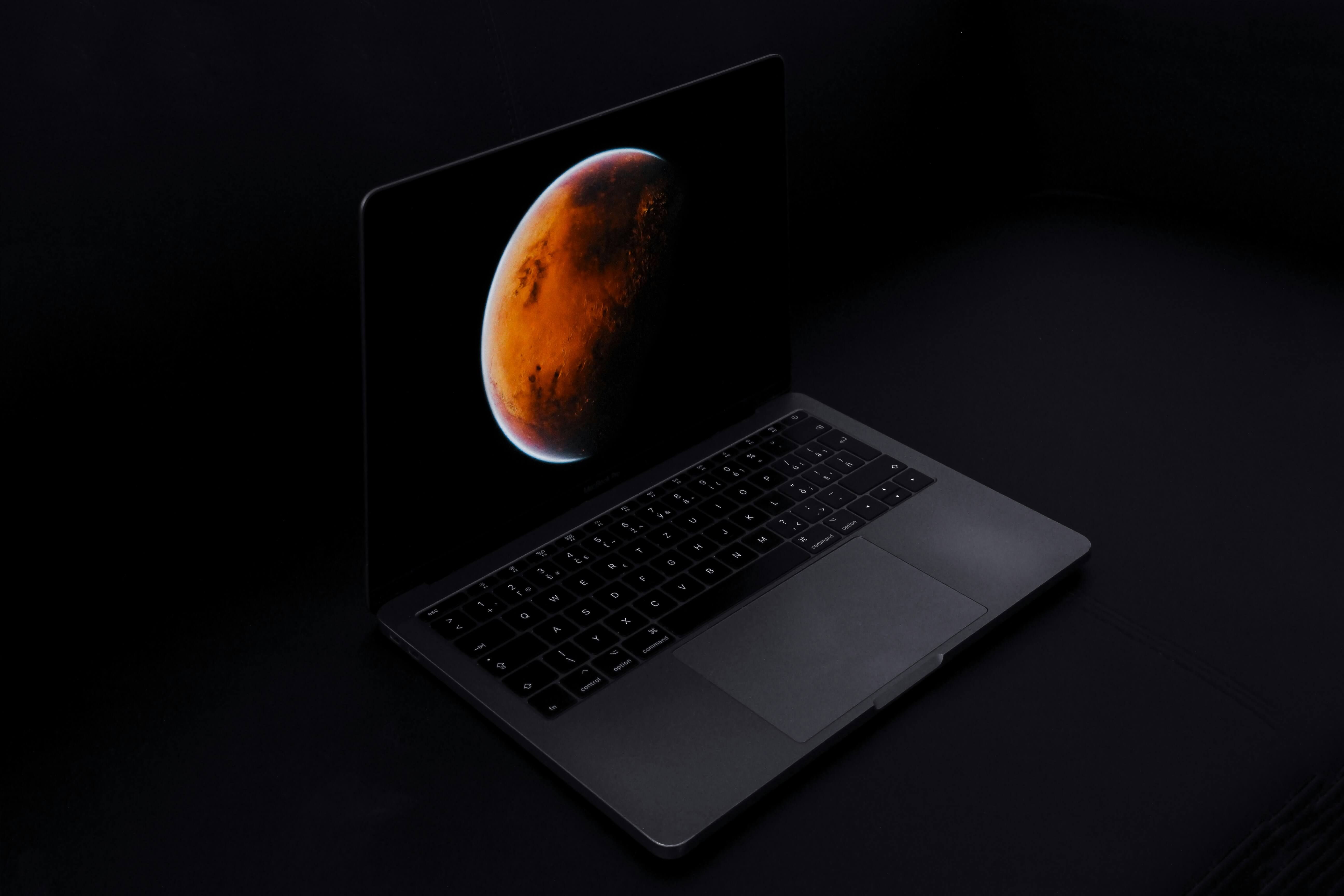 Space Gray laptop showing Mars against a starry night sky, lit by a desk lamp